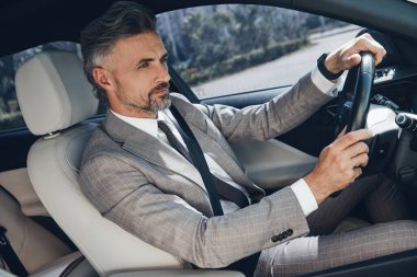 Handsome mature man in formalwear looking confident while driving a car
