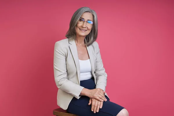 Confident Senior Woman Formalwear Smiling While Sitting Pink Background — Stockfoto