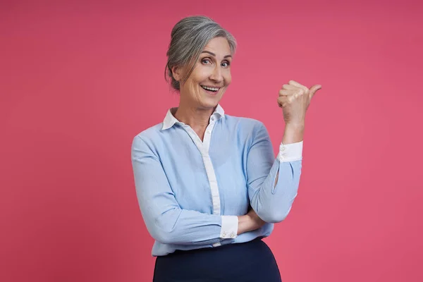 Happy Senior Woman Pointing Away While Standing Pink Background — Foto de Stock