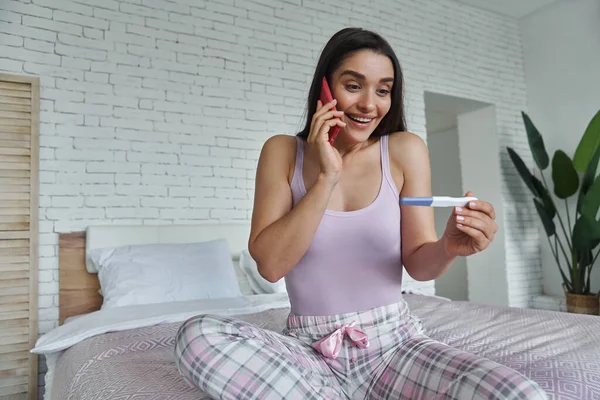 Excited Young Woman Holding Pregnancy Test Talking Mobile Phone While — Stock Fotó