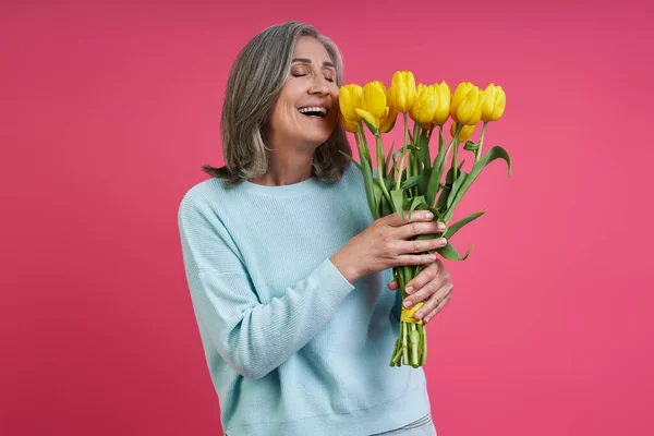 Happy Senior Woman Smelling Bunch Tulips While Standing Pink Background — Foto de Stock