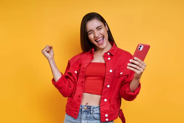 Excited Young Woman Holding Smart Phone Gesturing While Standing Yellow — Stockfoto