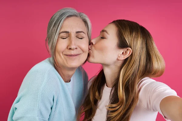 Adult Daughter Kissing Her Senior Mother While Making Selfie Pink — Foto Stock