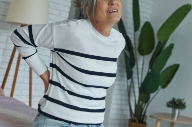 Close-up of senior woman suffering from backache while sitting on the bed at home