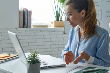 Confident woman using laptop while having web conference near the whiteboard at classroom