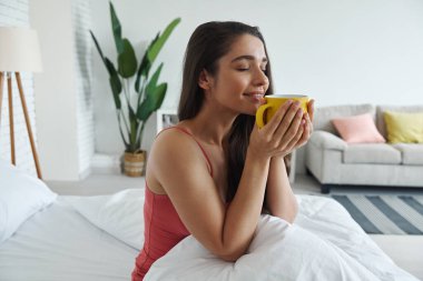 Attractive young woman enjoying coffee after waking up in bed