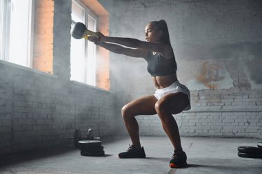 Full length of beautiful young African woman exercising with kettlebell in gym