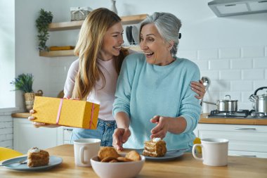 Surprised senior mother receiving a gift box from her daughter while both sitting at the kitchen