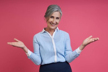 Happy senior woman gesturing while standing against pink background