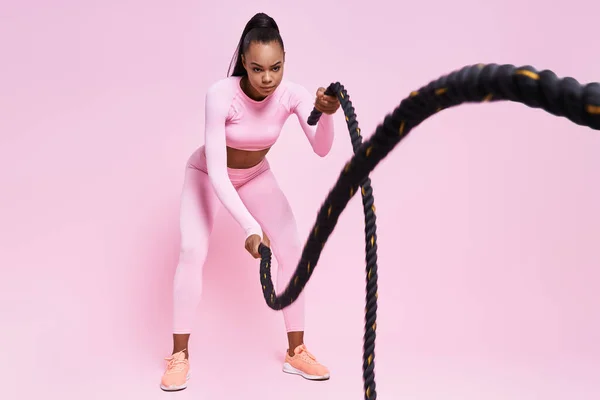 Confident Young African Woman Exercising Battle Ropes Pink Background — Stockfoto