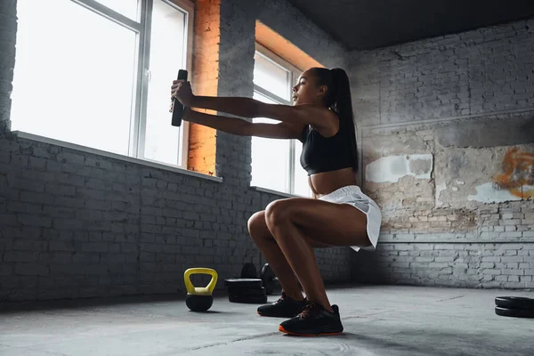 Concentrated young African woman lifting weights while exercising in gym