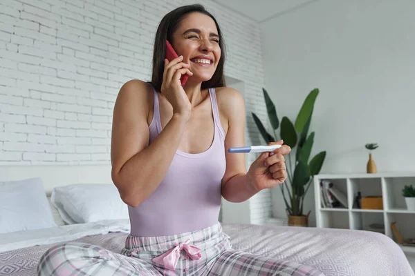 Excited Woman Holding Pregnancy Test Talking Mobile Phone While Sitting — Stock fotografie