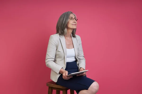 Thoughtful Senior Woman Formalwear Holding Digital Tablet While Sitting Pink — Fotografia de Stock