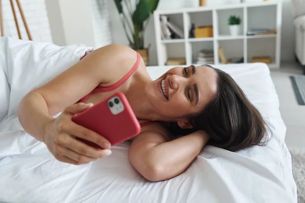 Happy Young Woman Holding Smart Phone While Lying Bed Home — Stockfoto