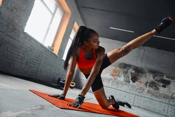 Beautiful young African woman doing stretching exercises in gym