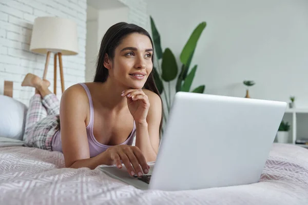 Thoughtful Young Woman Using Laptop While Lying Bed Home — Stock Photo, Image