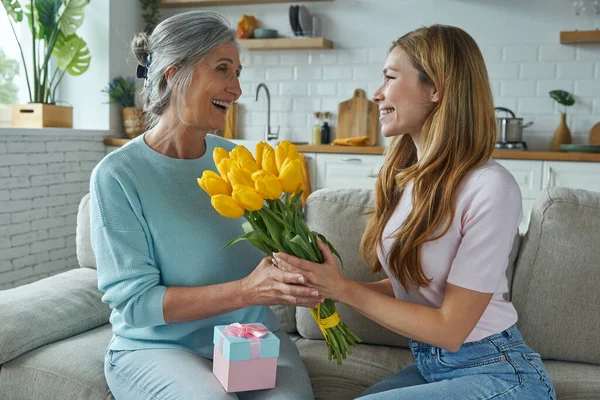 Surprised senior mother receiving a gift box and a bunch of tulips from her daughter