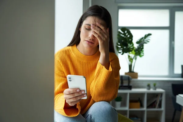 Depressed Woman Looking Her Smart Phone Touching Head While Sitting — Stockfoto