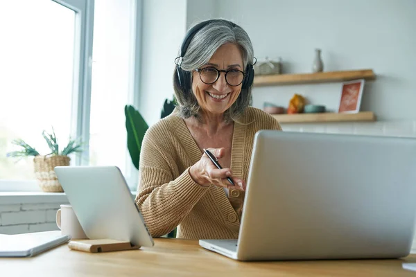 Happy Senior Woman Using Laptop Gesturing While Sitting Desk Kitchen — Foto de Stock