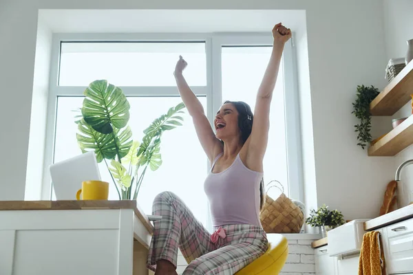Excited Woman Using Laptop Keeping Arms Outstretched While Sitting Kitchen — Stok fotoğraf