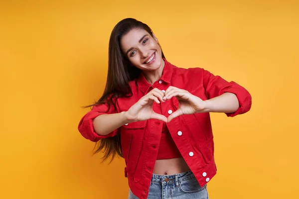 Beautiful Young Woman Gesturing Heart Shape Yellow Background — Zdjęcie stockowe