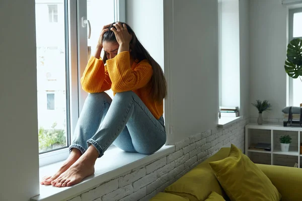 Frustrated Young Woman Holding Head Hands While Sitting Window Sill — Foto de Stock