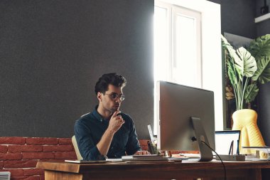 Confident young man using computer while sitting at his working place in office