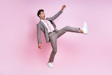 Excited young man in full suit smiling while moving against pink background