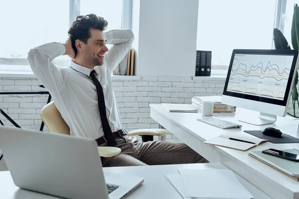 Relaxed man holding hands behind head while sitting at his working place in office