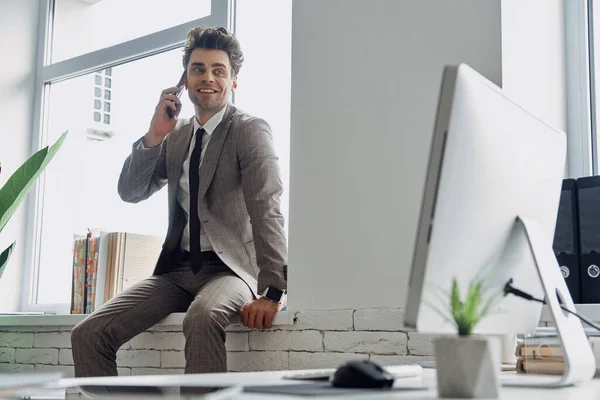 Счастливый Молодой Человек Разговаривает Мобильному Телефону Сидя Подоконнике Офисе — стоковое фото