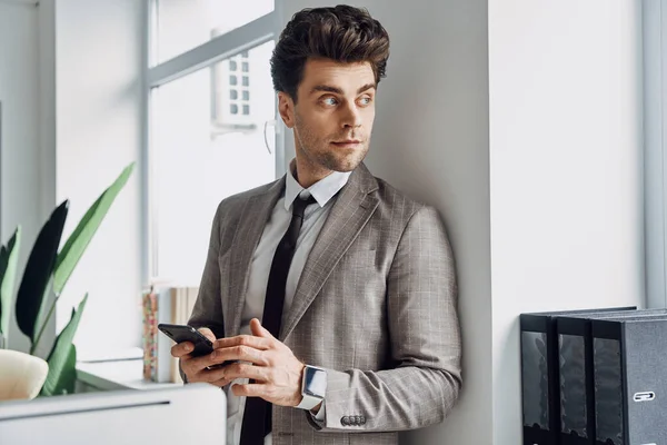 Handsome Young Man Holding Smart Phone Looking Window Office — ストック写真