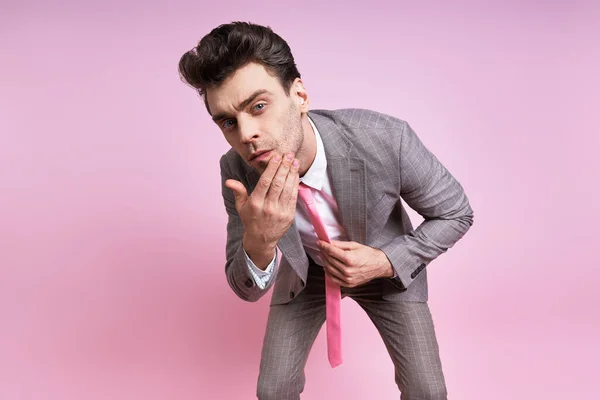 Handsome man in full suit touching his face while standing against pink background