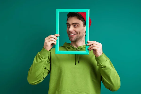 Playful Young Man Looking Picture Frame While Standing Green Background — Zdjęcie stockowe