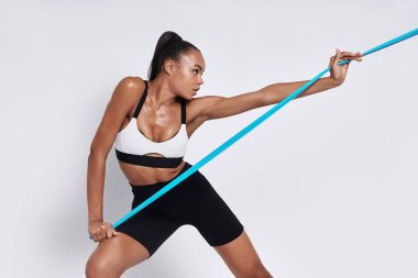 Active young African woman exercising with elastic resistance band against white background