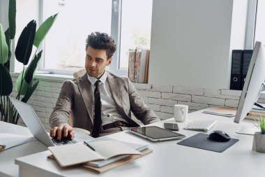 Handsome young man using computer while sitting at his working place in office