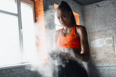 Concentrated African woman preparing hands with talcum powder before training in gym