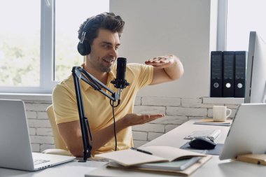 Good looking young man using microphone and gesturing while recording podcast in studio