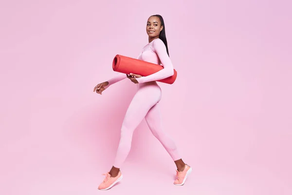 Beautiful African Woman Carrying Exercise Mat While Walking Pink Background — Fotografia de Stock