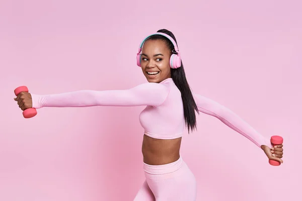 Cheerful African Woman Headphones Exercising Dumbbells Pink Background — Stock fotografie