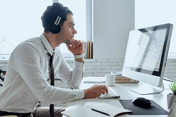 Concentrated man in headphones using computer while sitting at his working place in office