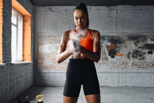 Beautiful African woman preparing hands with talcum powder before training in gym