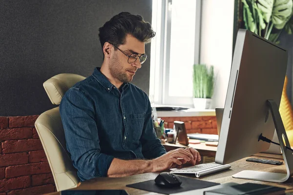 Handsome young man using computer while sitting at his working place in office