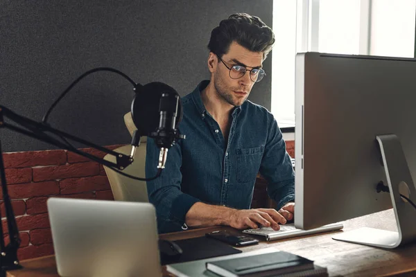 Confident young man using computer while sitting at radio station office