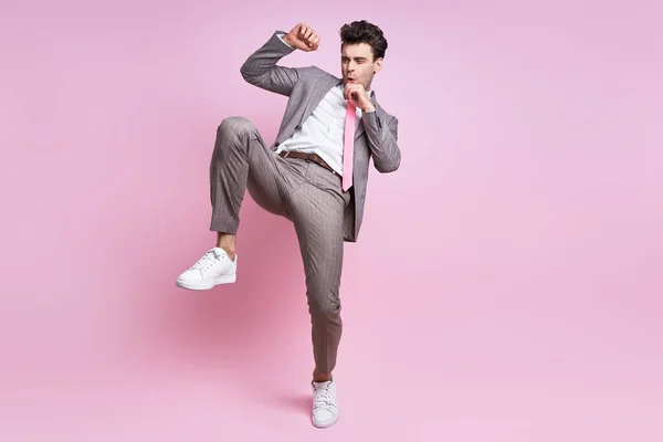 Furious young man in full suit fighting while standing against pink background