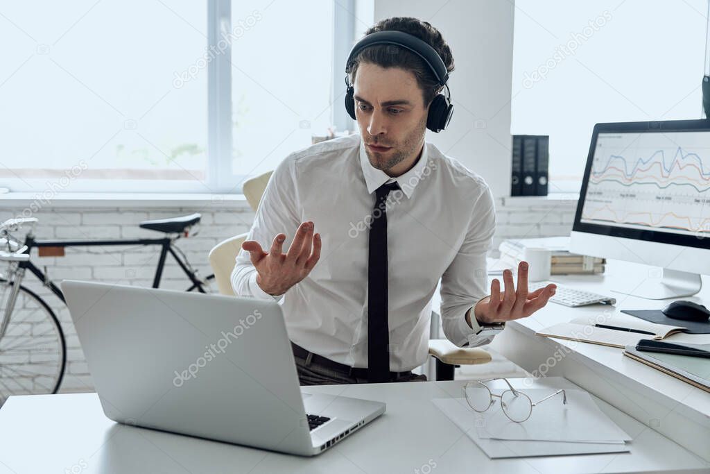 Handsome young man in headphones gesturing while having web conference in office