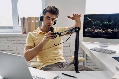 Confident man in headphones using microphone and gesturing while recording his business podcast
