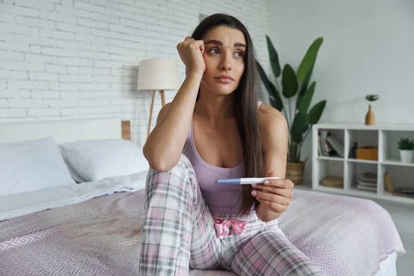 Depressed Young Woman Holding Pregnancy Test While Sitting Bed Home — Foto de Stock
