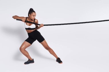 Confident young African woman pulling a rope against white background