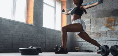 Unrecognizable young woman using elastic resistance band while exercising in gym