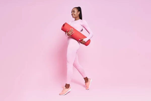 Happy African Woman Carrying Exercise Mat While Walking Pink Background — 图库照片